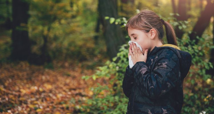 girl blowing her nose in fall in the woods