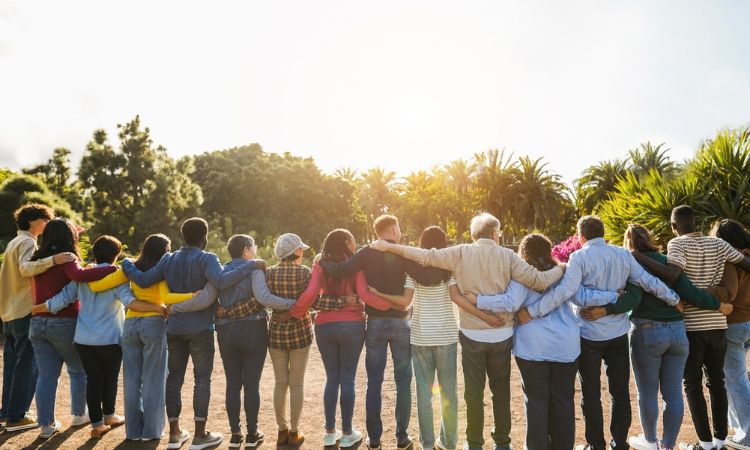 a large group of people standing side by side arms around each others shoulders facing the sun