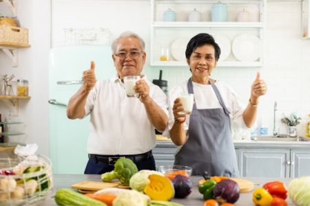 couple drinking milk and standing in kitchen in front of vegetables