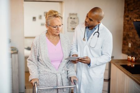 older woman using a walker speaking w a doctor