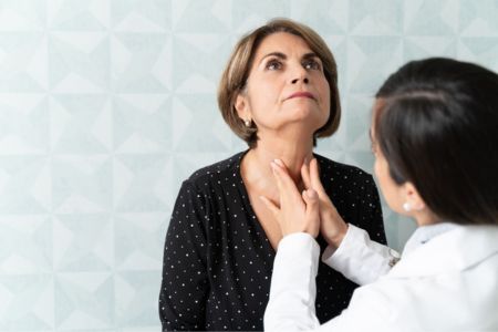 female doctor giving a female patient a thyroid exam by touching her throat