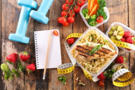 healthy food, hand weights measuring tape and note pad on a table