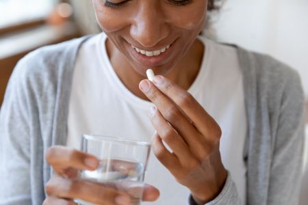 female smiling and taking a multivitamin with a glass of water 