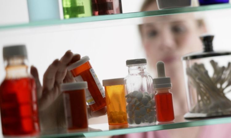woman looking into a medicine cabinet, reading prescription bottles