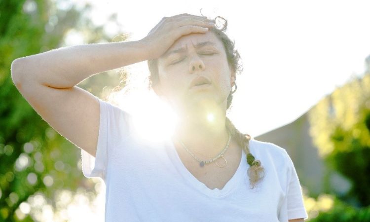 woman out doors with her hand on her head, seemingly being impacted by the heat from the sun
