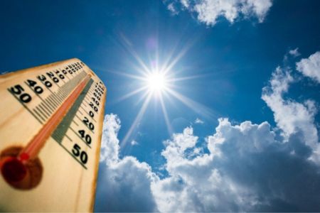 an upward shot of a thermometer with the sky and sun in the background