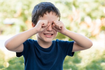 young boy rubbing itchy eyes outdoors 