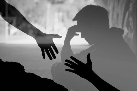 silhouette of a man sitting stressed out with hands reaching down to help him 