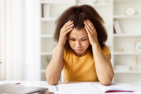 woman looking overwhelmed with her hands on her head, seated at a desk at home 