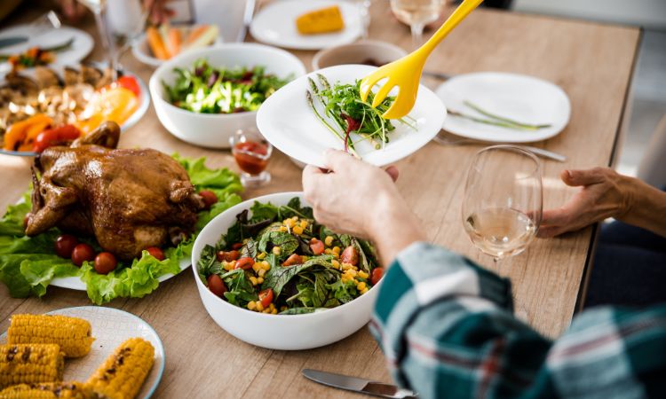 a person serving food from a full thanksgiving dinner table