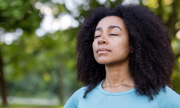 young woman standing outside, eyes closed and calm