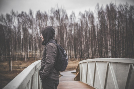 A young man standing on a bridge looking out solemnly 
